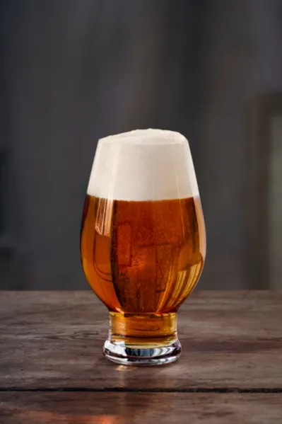 Tulipanformet glass med ravfarget øl og tykt hvitt skum på et rustikt trebord.