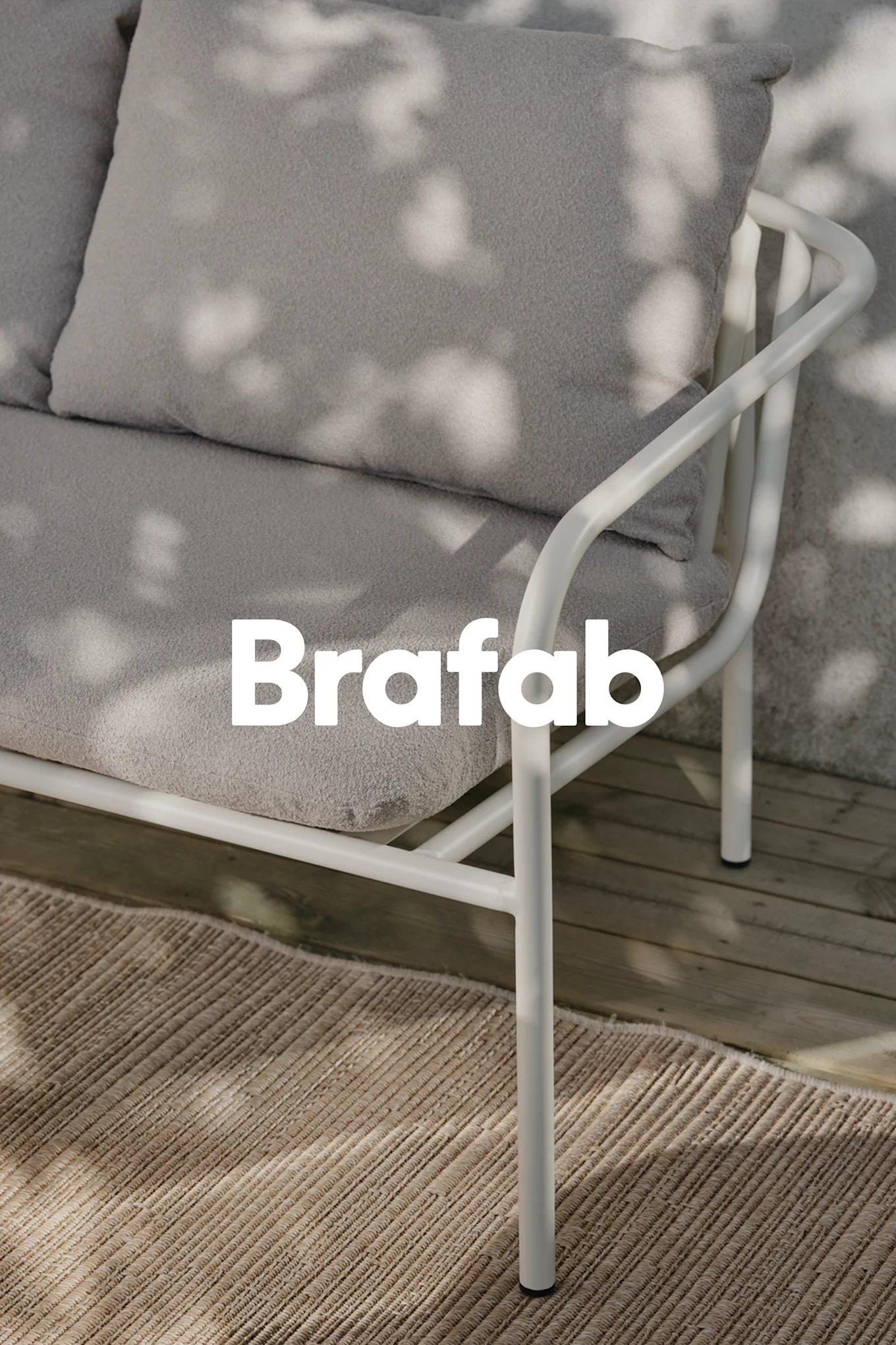 Brafab-logo over lys grå utendørssofa, hvit metallramme, på beige teppe på treterrasse med flekkete skygger.