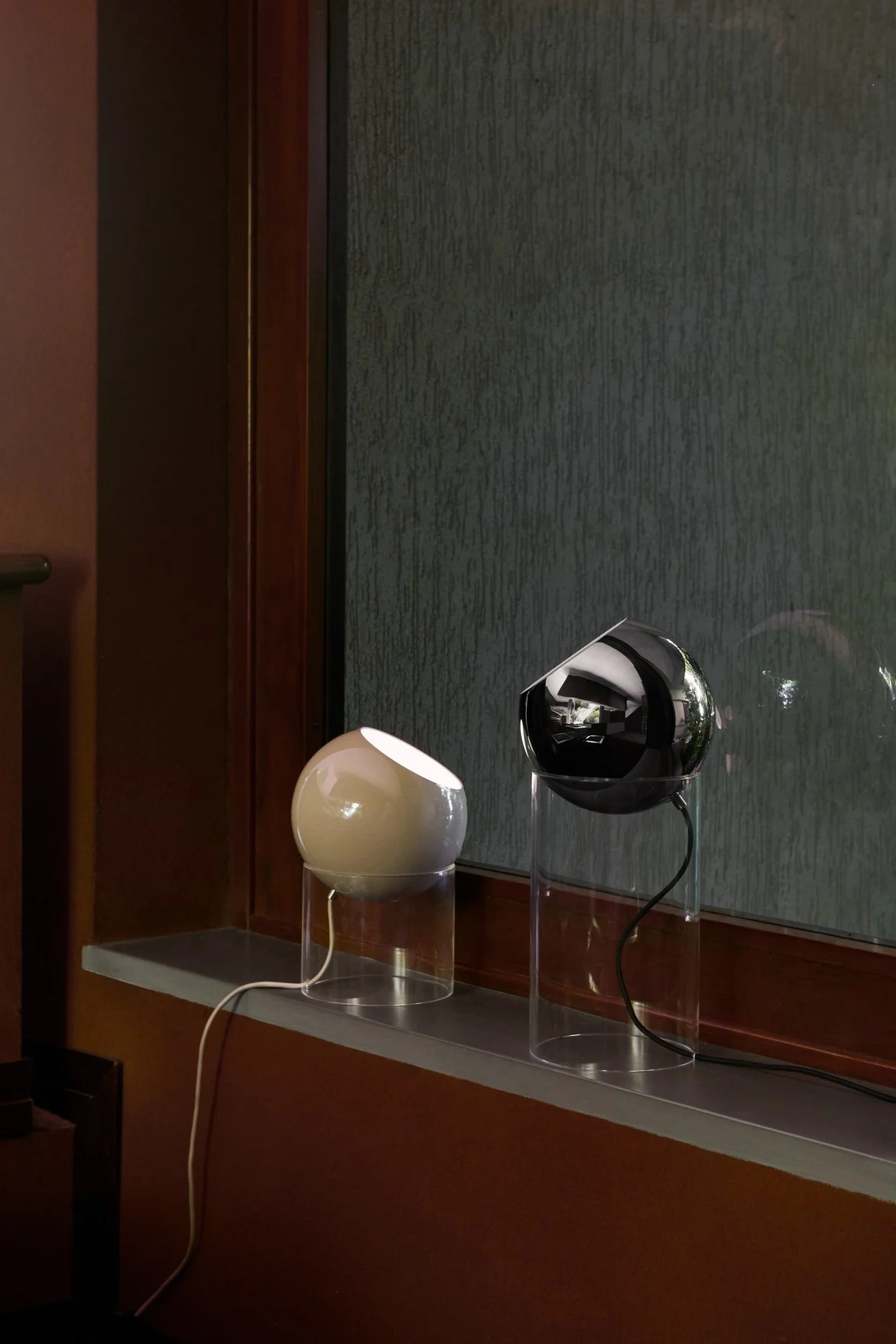 I en vinduskarm står to Topan bordlamper i ulike størrelser fra &Tradition, i beige og svart.
