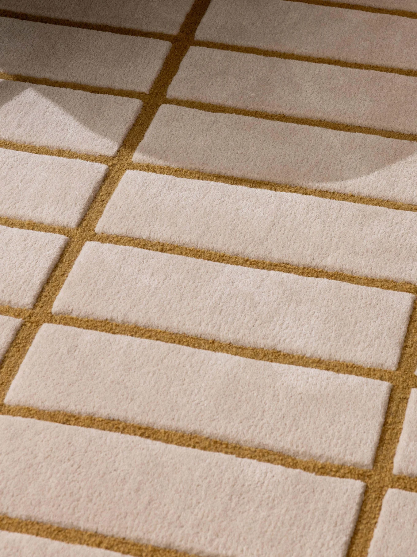 Mønstret beige og gyllenbrunt teppe, grønt lenestolbein og et brett med hvit tekanne og kopp.