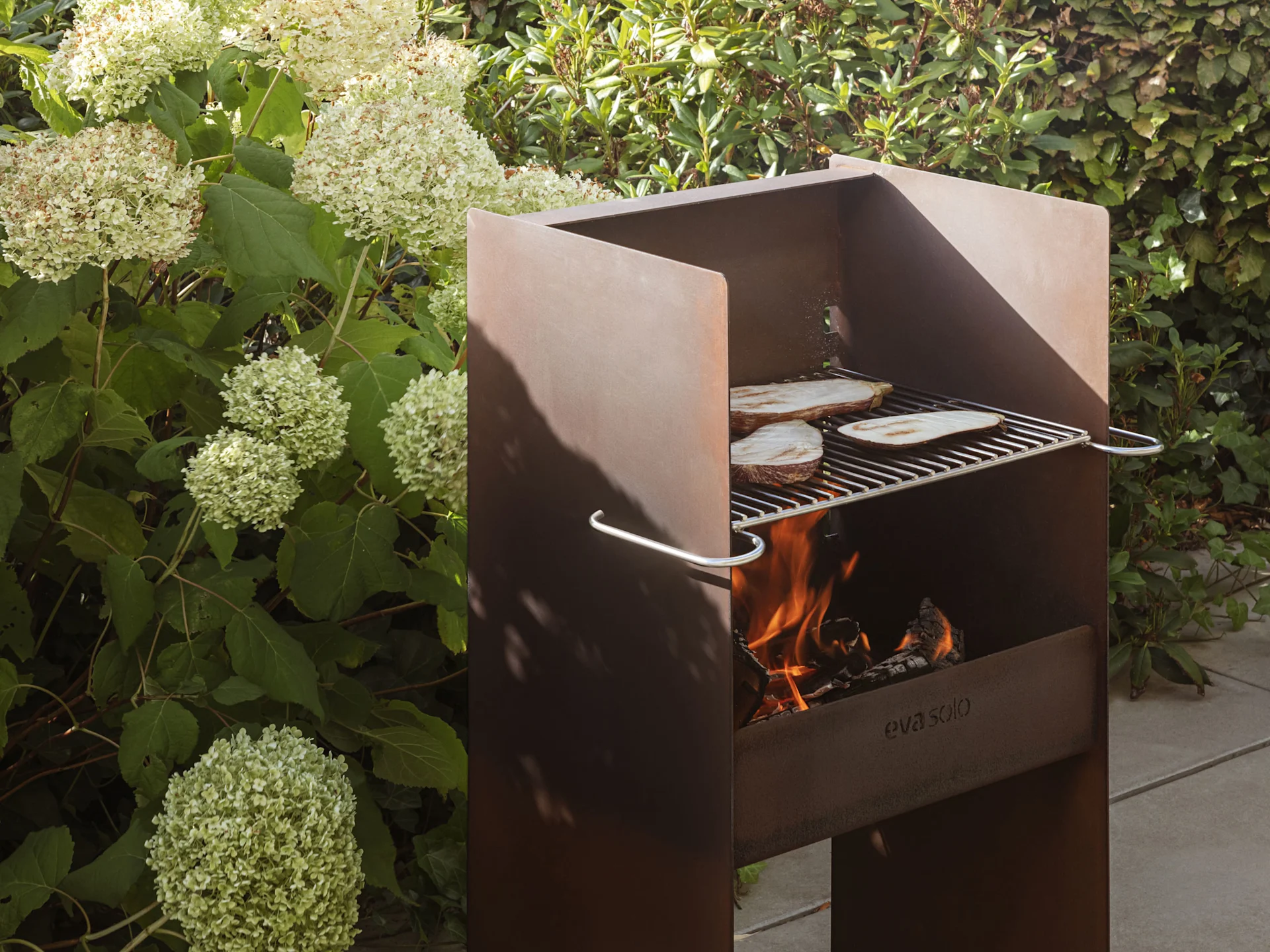 En rustikk utendørs metallgrill med flammer og aubergineskiver som steker på risten.