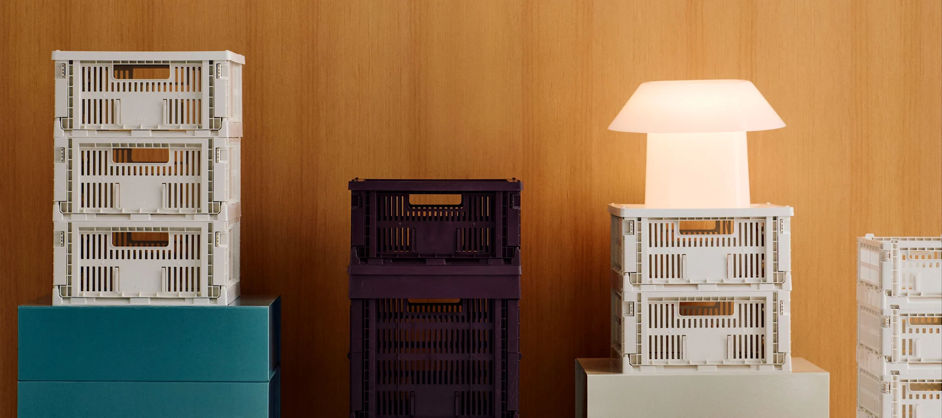 Stablar med kvite og mørkelilla samanleggbare kassar med ei lysande kvit moderne lampe på ein trebakkgrunn.