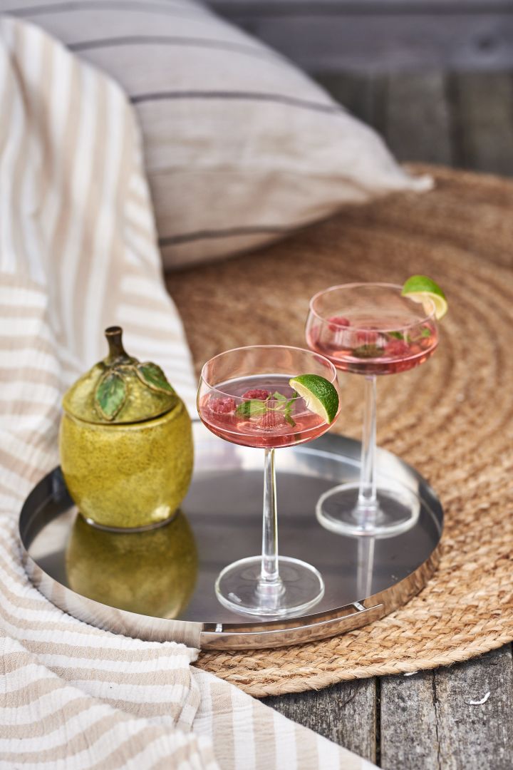 Iittala Essence cocktailglass med en god sommerdrink i på et sølvbrett på et juteteppe ved sjøen. 