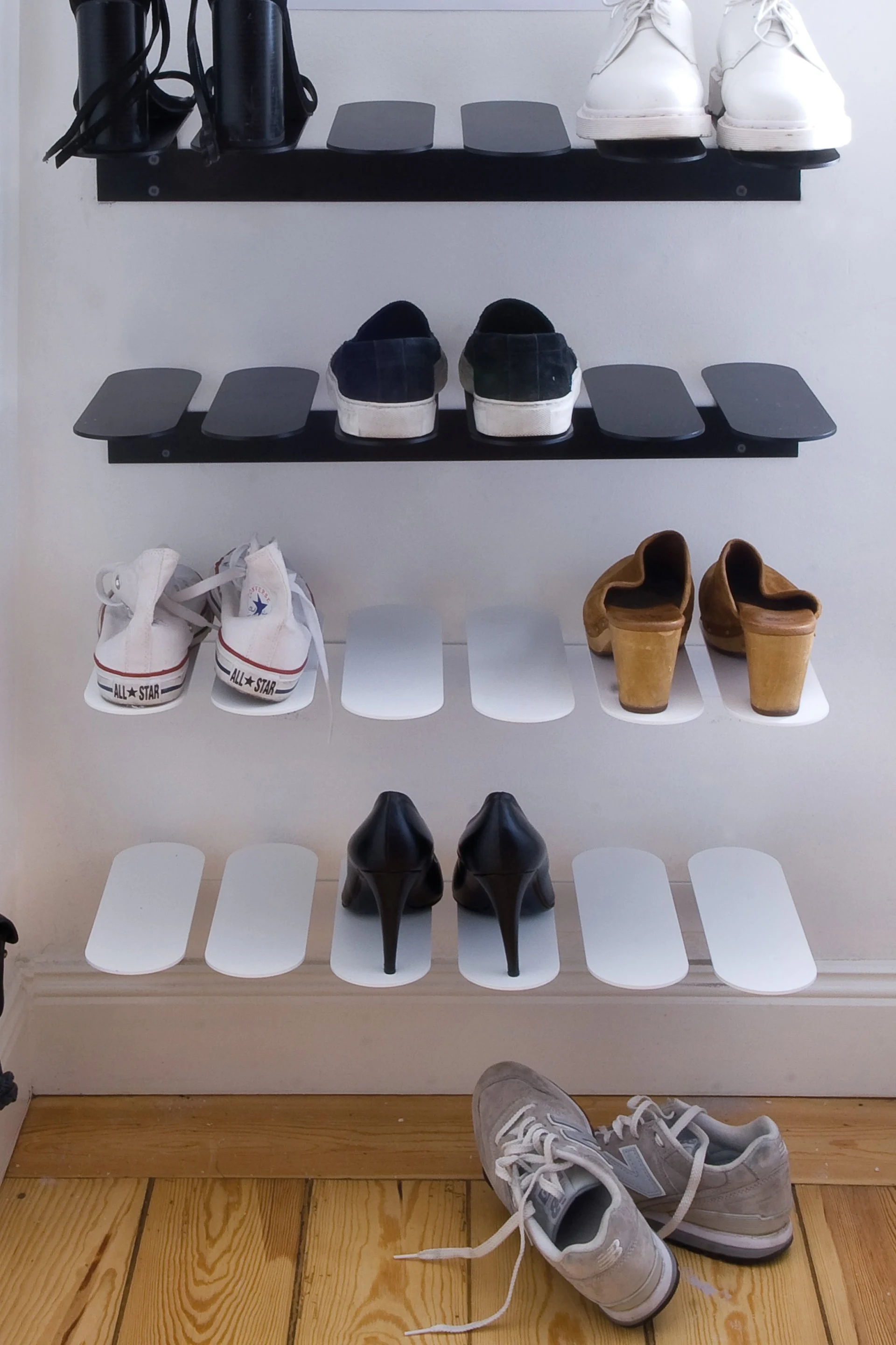 Diverse sko utstilt på veggmonterte hyller, inkludert svarte hæler, hvite joggesko, mørke slip-ons, tresko og grå joggesko.