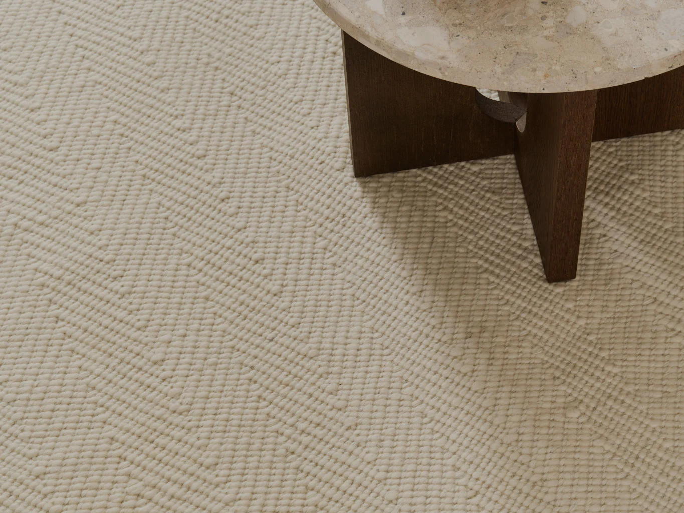 Nærbilde av et kremfarget teksturert teppe med chevronmønster, ved siden av et bord med steinplate.