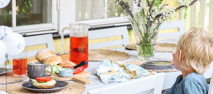 Bilde som viser en liten gutt sittende ved et dekket frokostbord med nybakte kaldhevede rundstykker.
