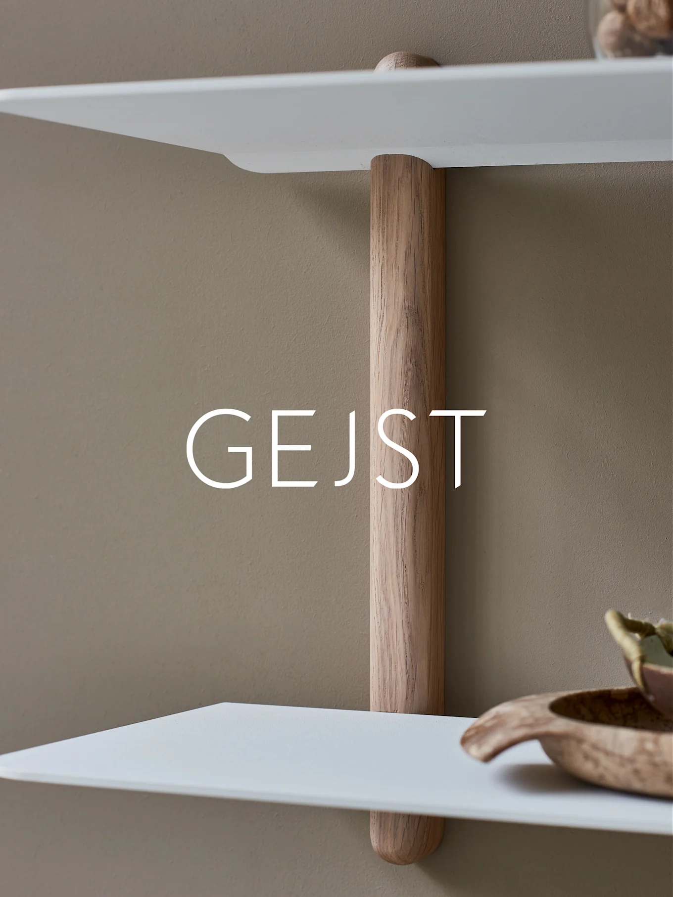 To hvite, avrundede hyller forbundet med en vertikal lys trestøttestang mot en beige vegg. En treskål er på den nedre hyllen.