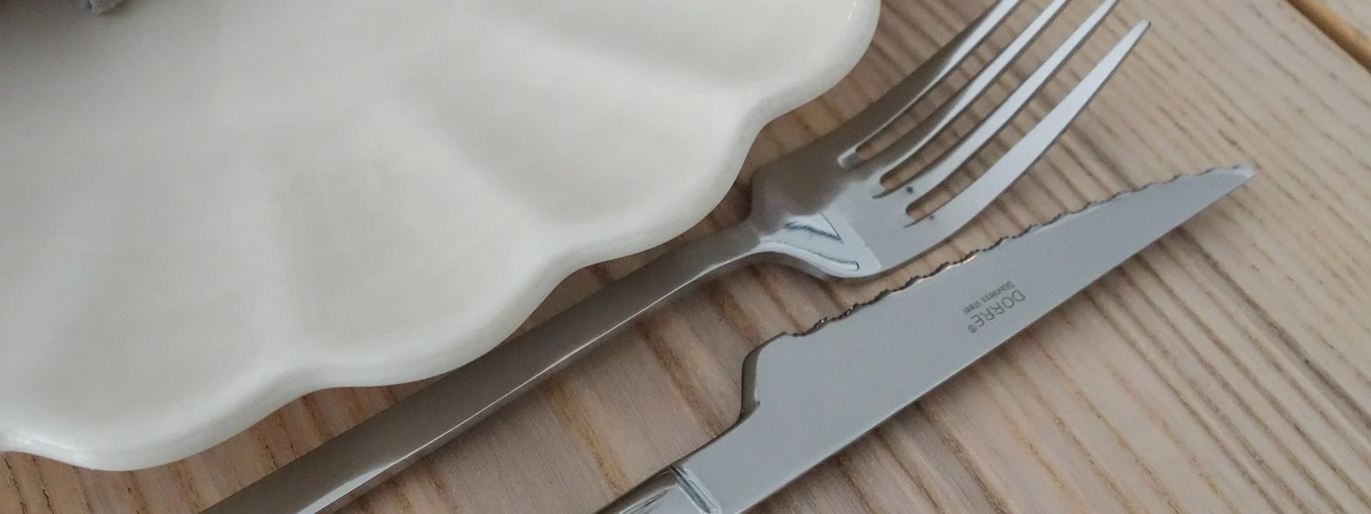 Elegant borddekking med en hvit riflet tallerken, grå linserviett, gull serviettring, sølvgaffel og -kniv, og et vinglass på et trebord.