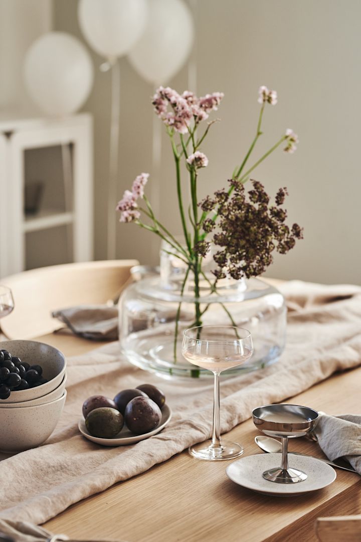 En romantisk middag hjemme blir enda bedre med riktig borddekking. Her ser du et enkelt dekket bord med glass fra Essence-kolleksjonen fra Iittala og en vase med blomster.