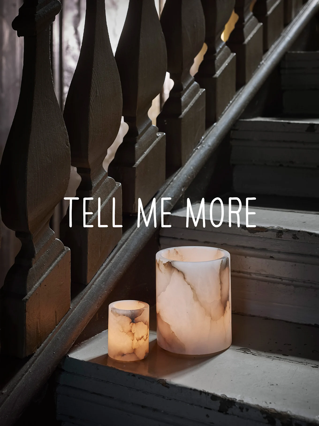 To glødende onyks-lignende lysestaker på en slitt tretrapp, med teksten "TELL ME MORE".