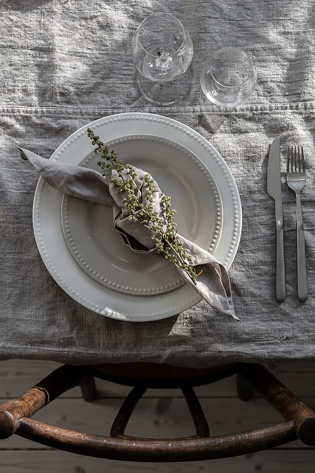 Hvordan brette servietter - her ser du en grå serviett brettet til en rustikk knute med en blomst fra hagen.