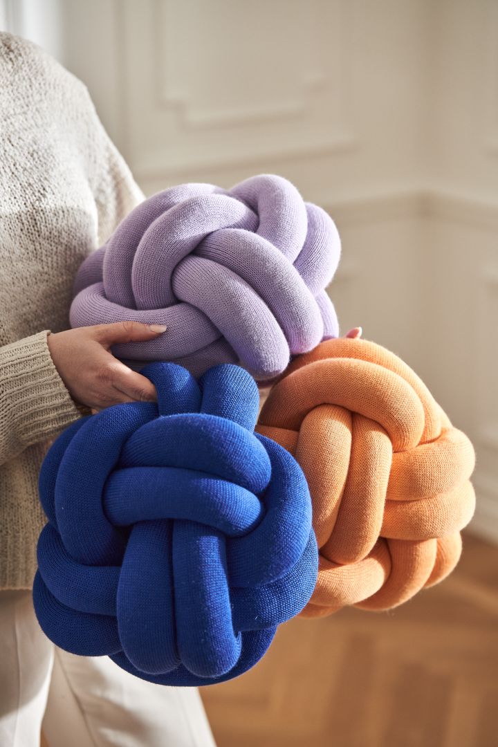 Knot-puter fra Design House Stockholm i blått, lilla og aprikos i armene til en kvinne.