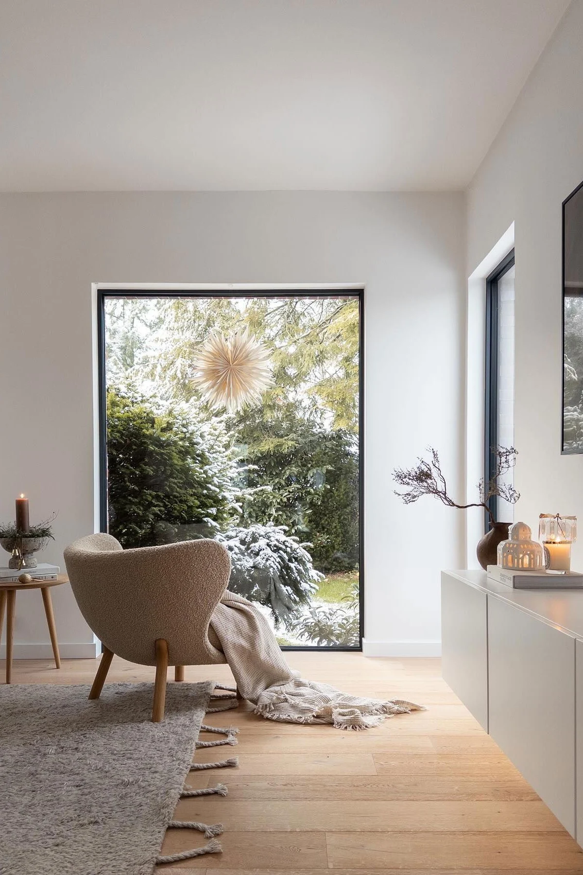 En stue med svært minimalistisk julepynt. En julestjerne henger i vinduet med et stearinlys ved siden av.
