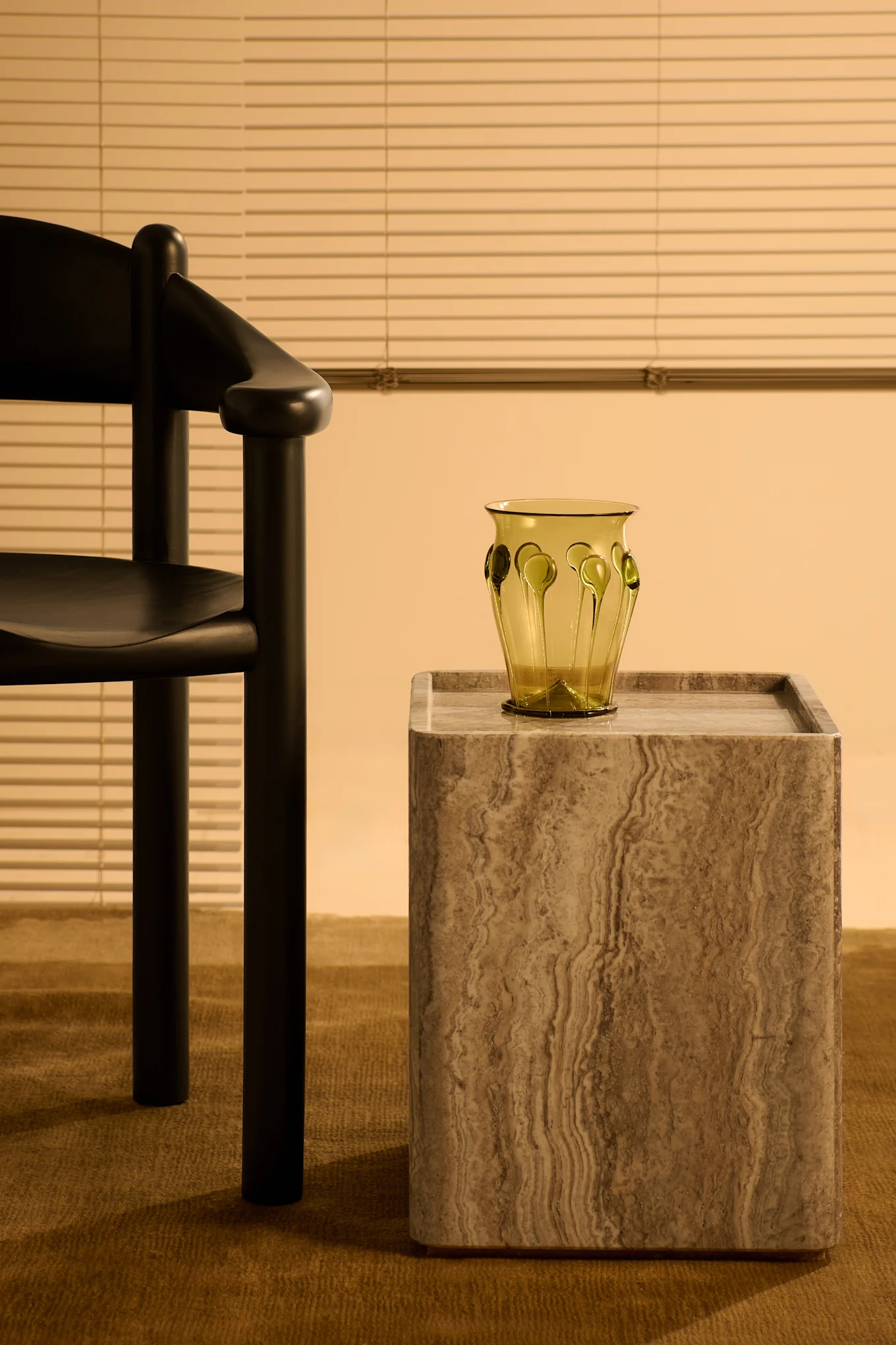 Sidebord i travertin fra Gubi og stol i svart furu, også fra Gubi – helt i tråd med interiørtrender 2025.