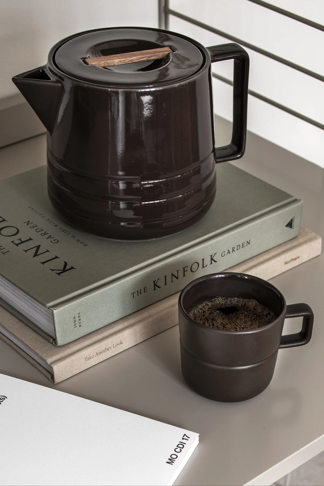 Mørkebrun keramisk kaffekanne med trekant, matchende krus med kaffe og to bøker.