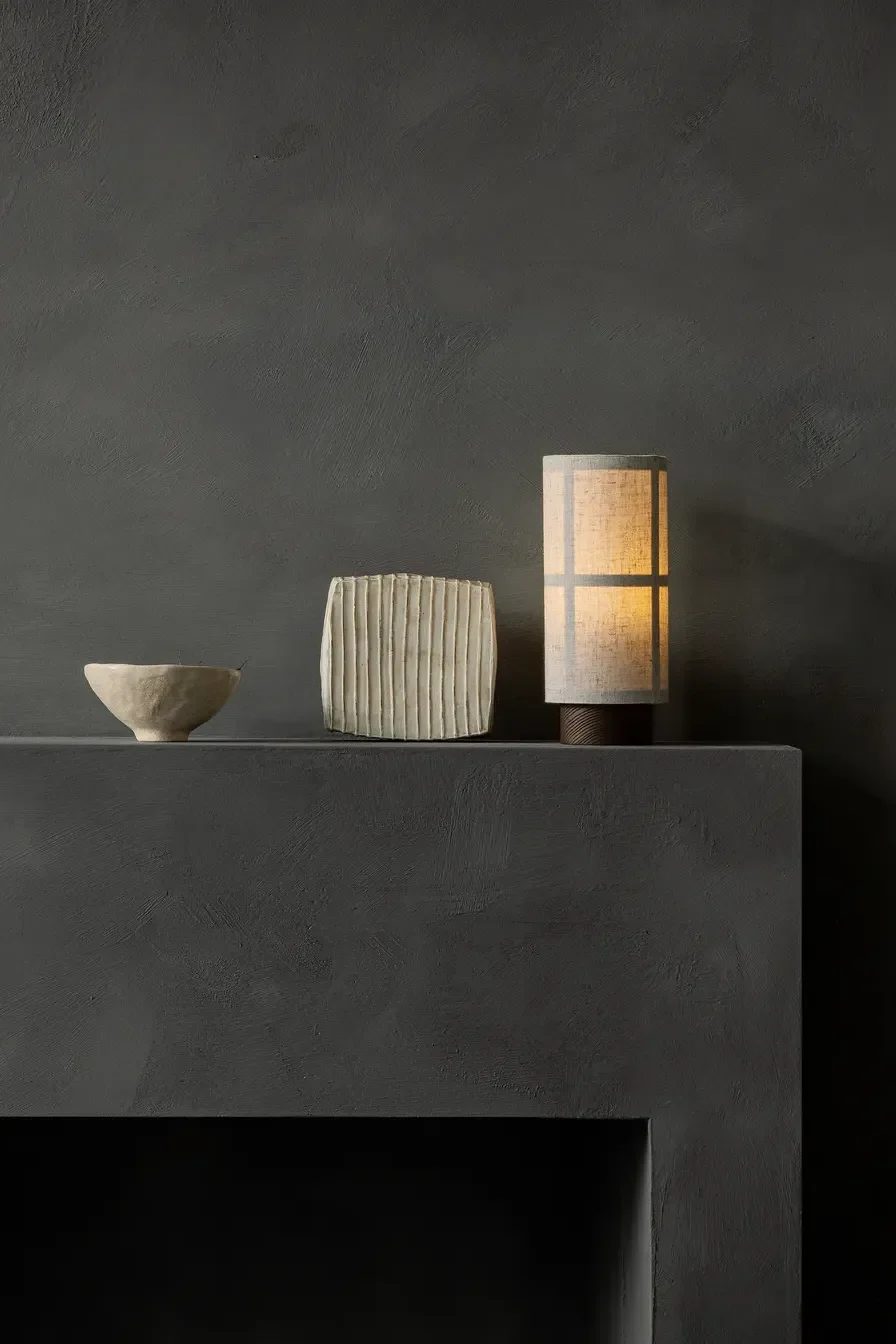 Tre dekorative gjenstander på en mørkegrå hylle: en beige bolle, en riflet kremfarget rektangel og Hashira oppladbar lampe fra Audo Copenhagen.