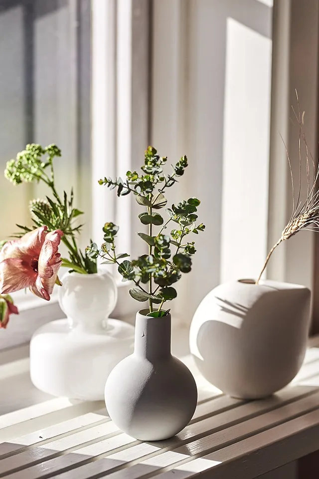 Flere små vaser for snittblomster står i en vinduskarm. 