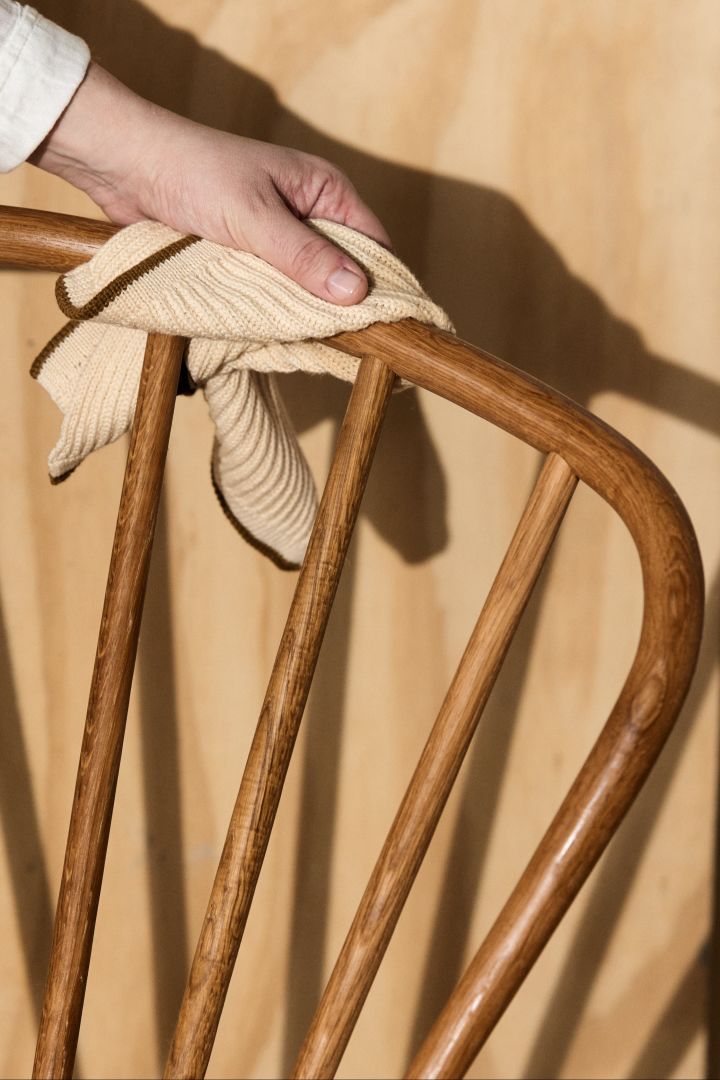 Her ser du en hånd som rengjør et teakmøbel med en klut.
