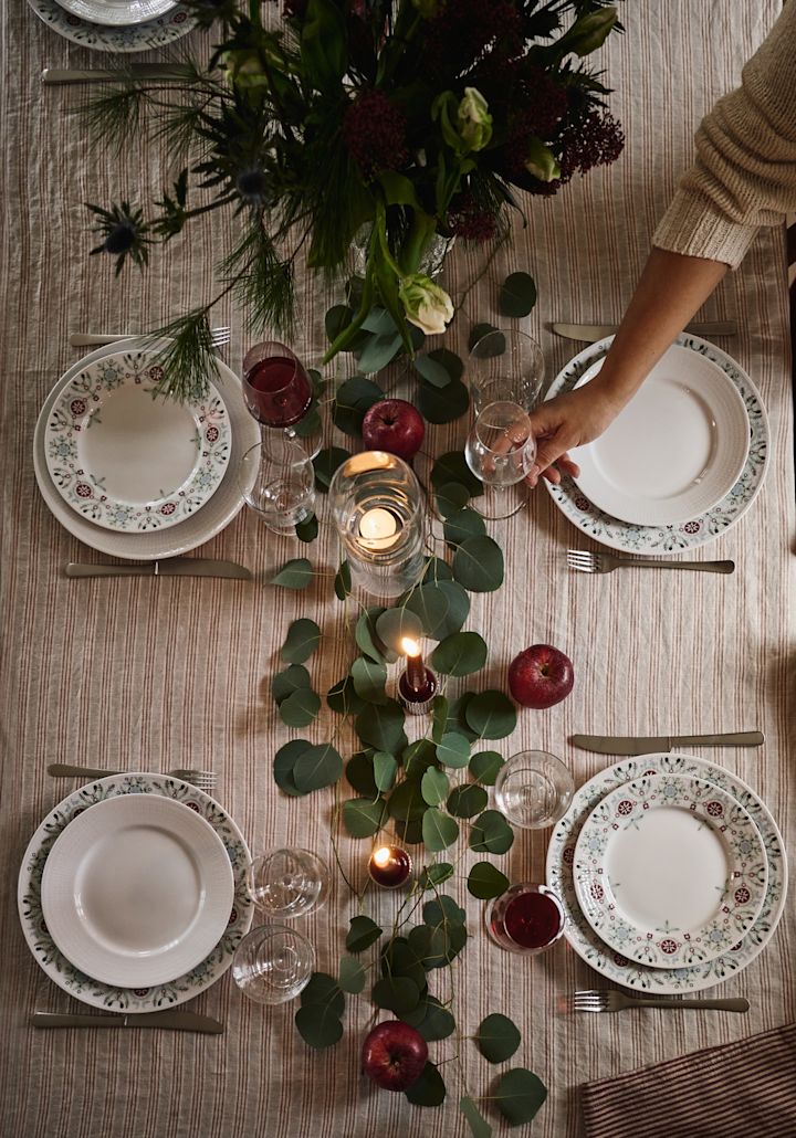 En enkel og elegant idé til juleborddekking fotografert ovenfra med grønne blader og røde epler som dekorasjon. 