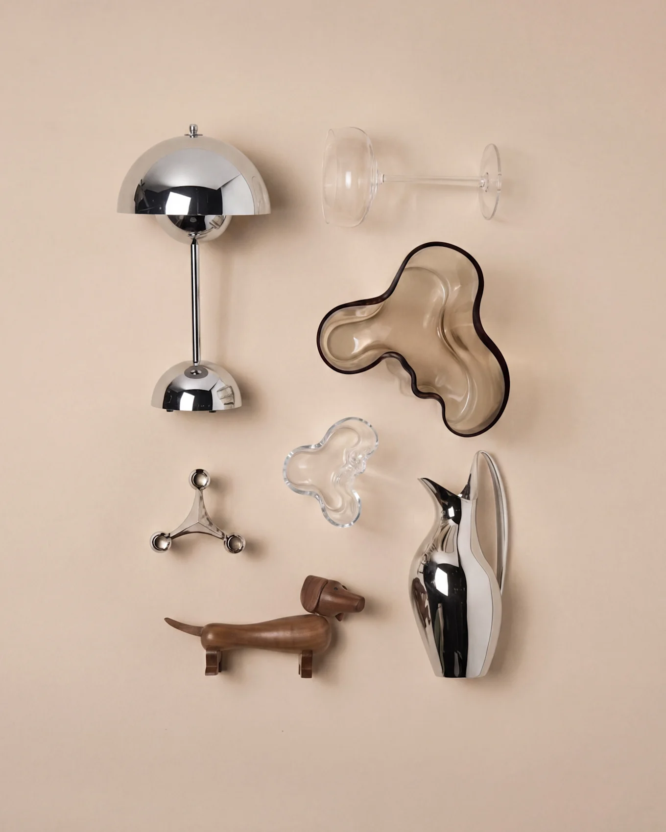 Moderne interiør: krom sopplampe, klart vinglass, brun bølget bolle, sølv lysestake, tre dachs, sølvkanne.