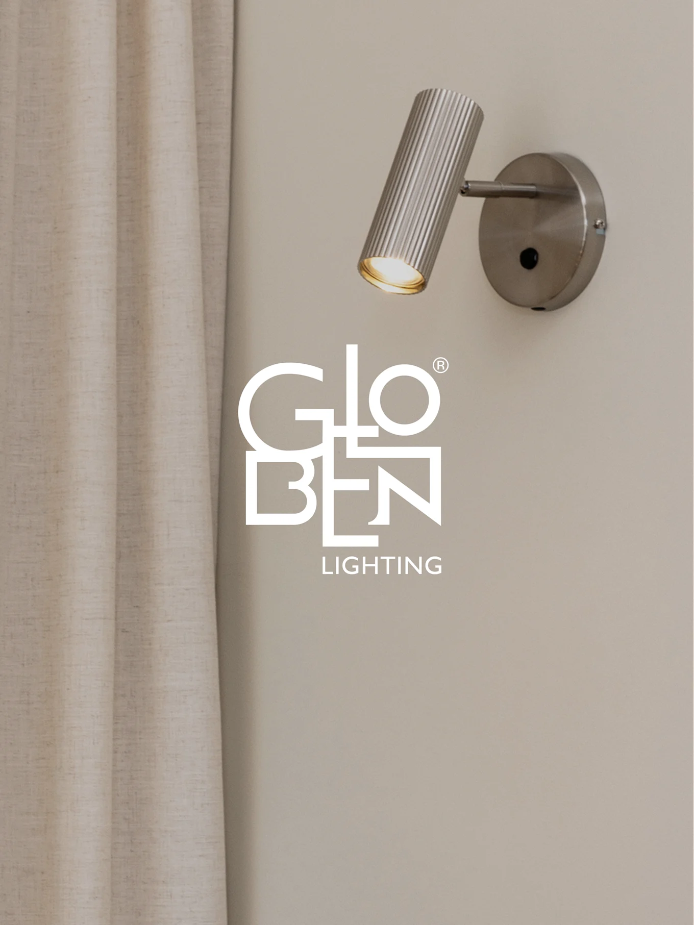 En børstet metall, ribbet veggspotlight med et varmt lys, ved siden av en lys gardin, med Globen Lighting-logoen.
