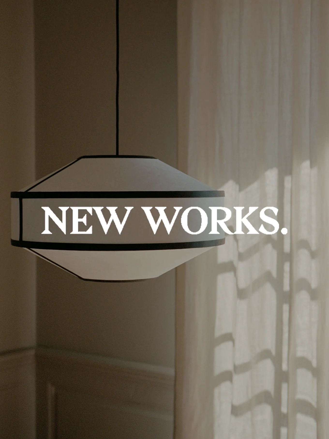 En bred, hvit pendellampe med mørk kant henger, med teksten 'NEW WORKS.' overlagret. Sollys kaster skygger på et gardin.