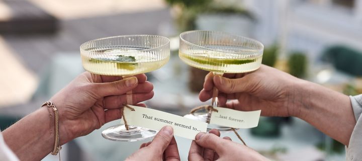 Bordkort med sommersanger knyttet rundt bunnen av Ripple champagneglasset fra Ferm Living er et smart tips til hagefesten.