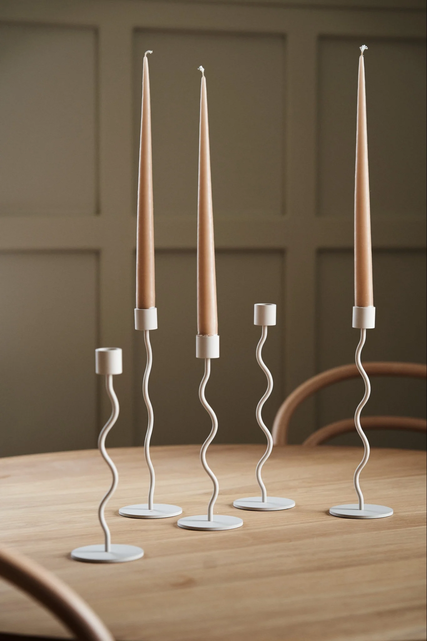 En samling av Curve-lysestaker i beige fra Cooee Design på et spisebord i tre.