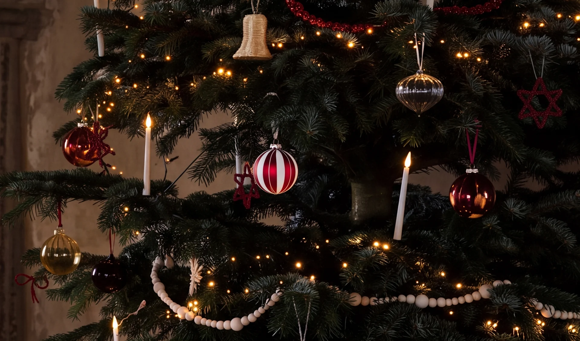 Et pyntet juletre med varme lys, røde, sølv og gull julekuler, hvite stearinlys og treperlegirlandere.