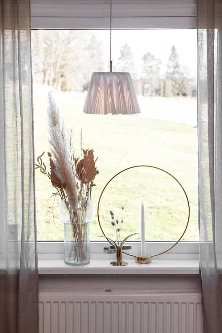 Pynt vinduskarmen: Et vindu med gardiner, en vase med tørkede blomster og lysestaken Gloria fra Klong.
