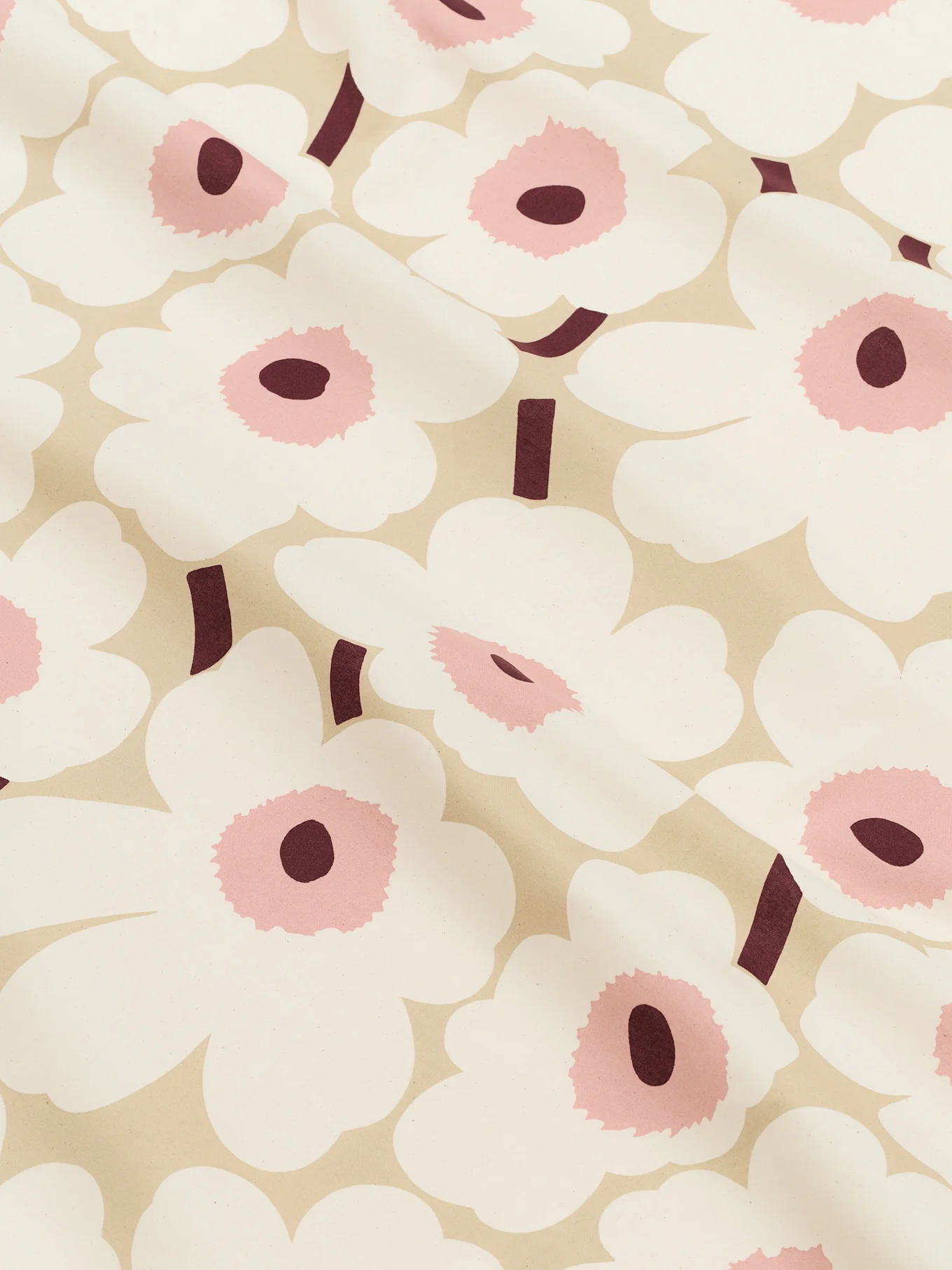 Nærbilde av et lys beige stoff mønstret med store hvite stiliserte blomster med rosa sentre og mørke burgunderstengler.
