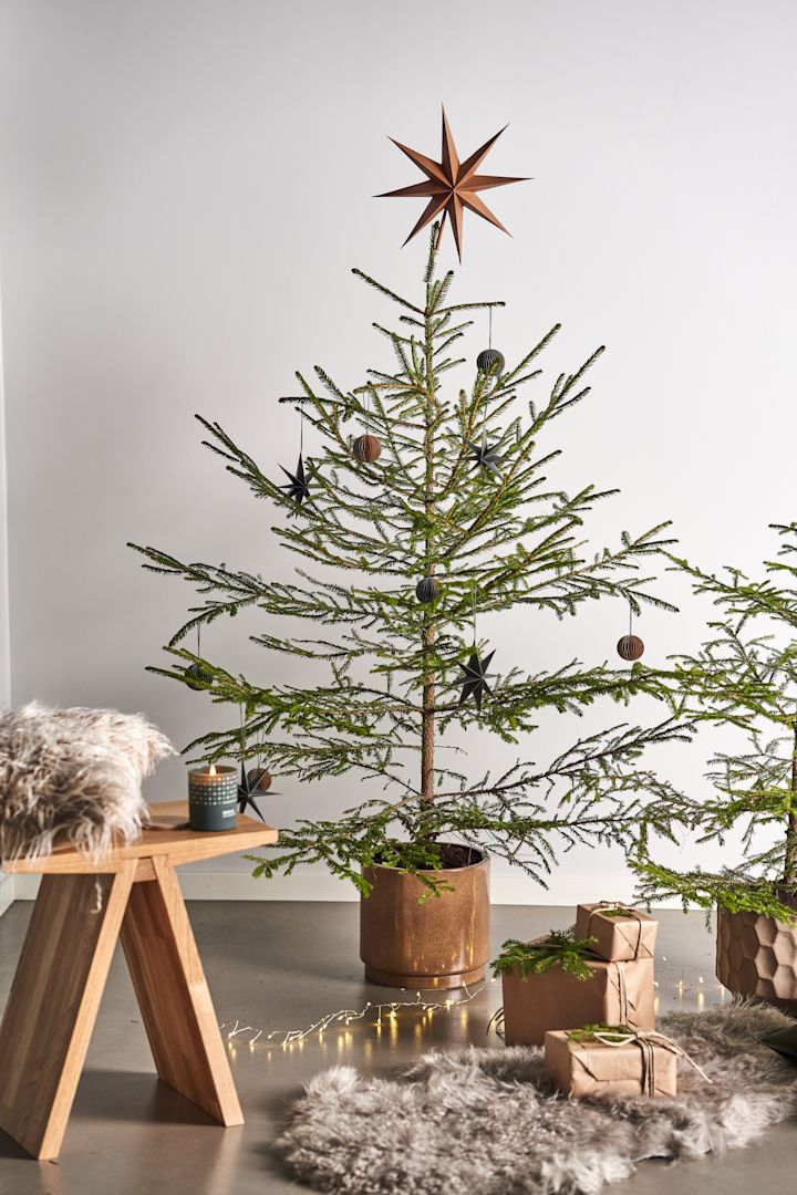 Pynt juletreet med juletrepynt i 4 forskjellige stiler i henhold til Nest Trends - Nurture, Share, Boost and Cultivate. Her ser du Angle krakk fra Muubs med et Skandinavisk duftlys i Forest duften ved siden av pakker på et saueskinnsteppe.