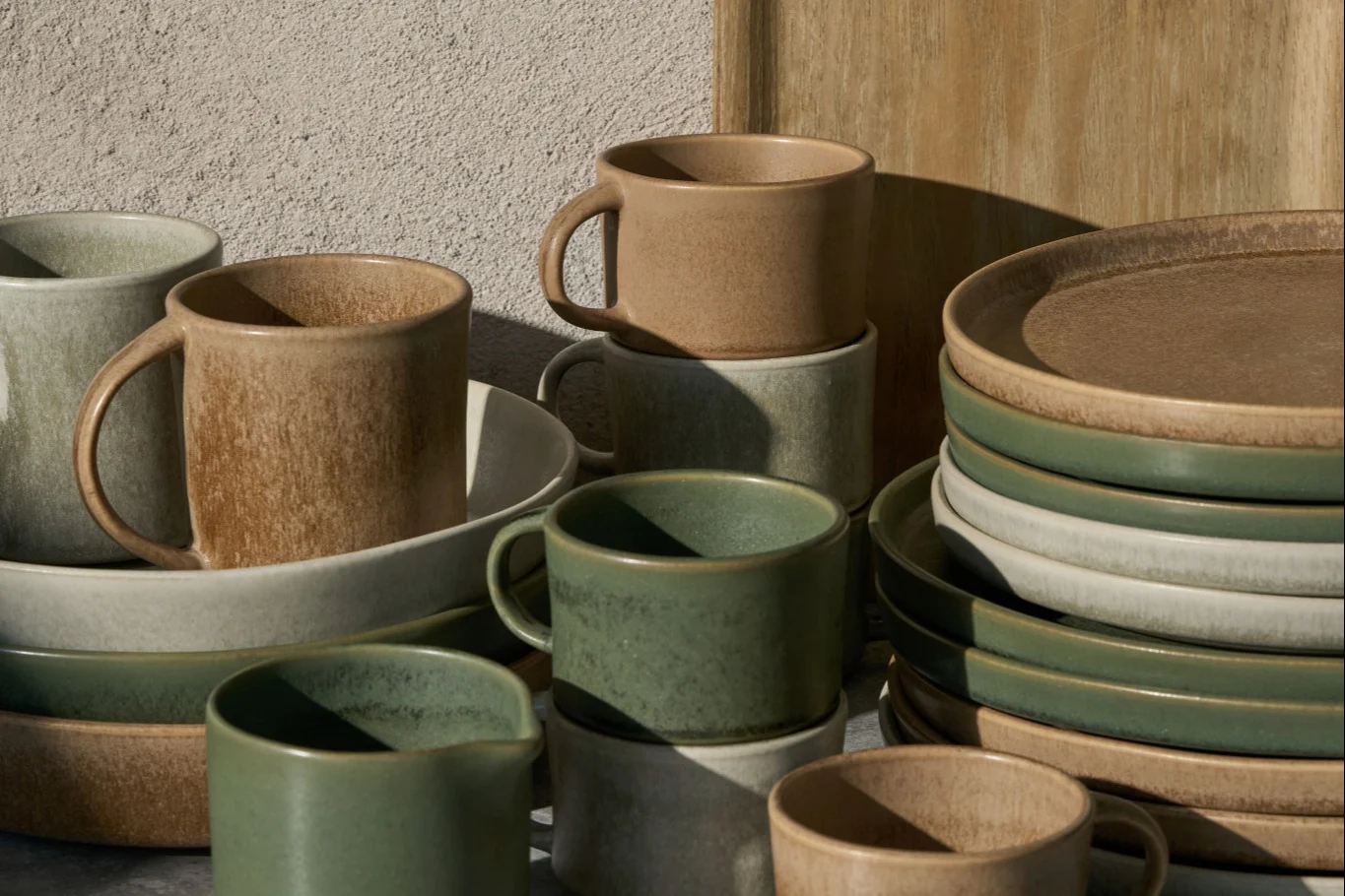 Stablede keramikkrus, boller og tallerkener i beige, lys grå og salviegrønn, med en rustikk finish.