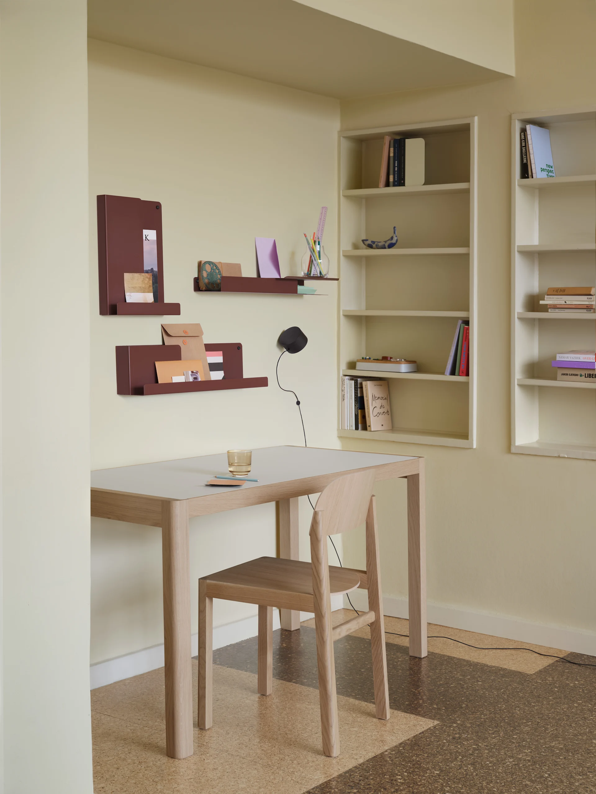 Et minimalistisk kontoroppsett med lyst trebord, stol, rødbrune veggorganisatorer og innebygde bokhyller.