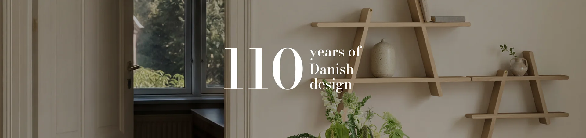 Teksten '110 years of Danish design' over et interiørbilde av et rom med en geometrisk trehylle, en vase og blomster.