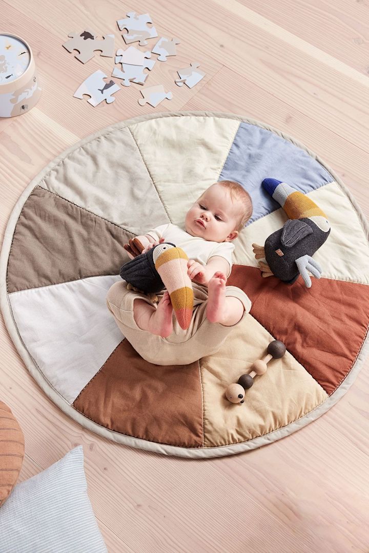 Kosebamsen Trine Tourca fra OYOY ligger ved siden av en baby på Moni barneruggen. Den myke bamsen er en flott og bærekraftig gave til babyshower.