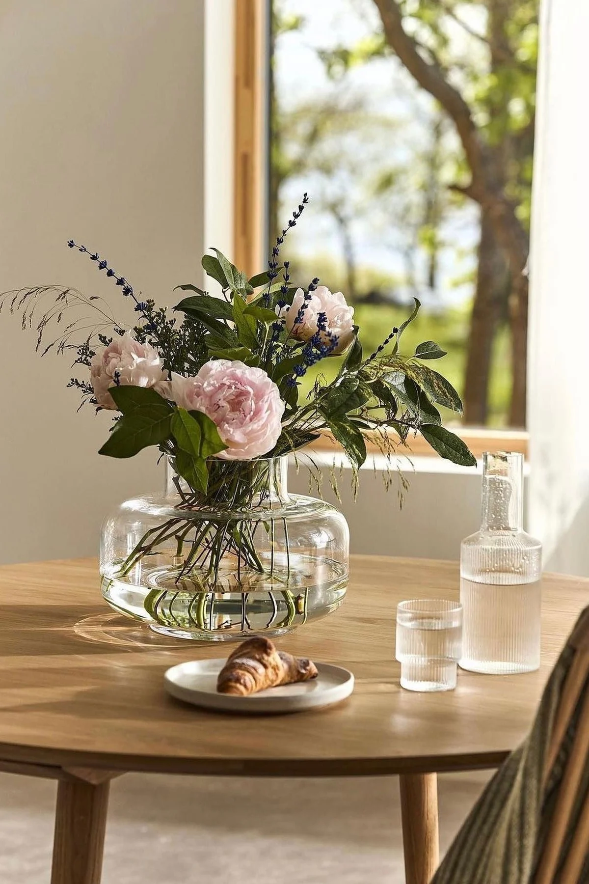 På et bord dekket med karaffel og croissant står Urna-vasen fra Marimekko med peoner.