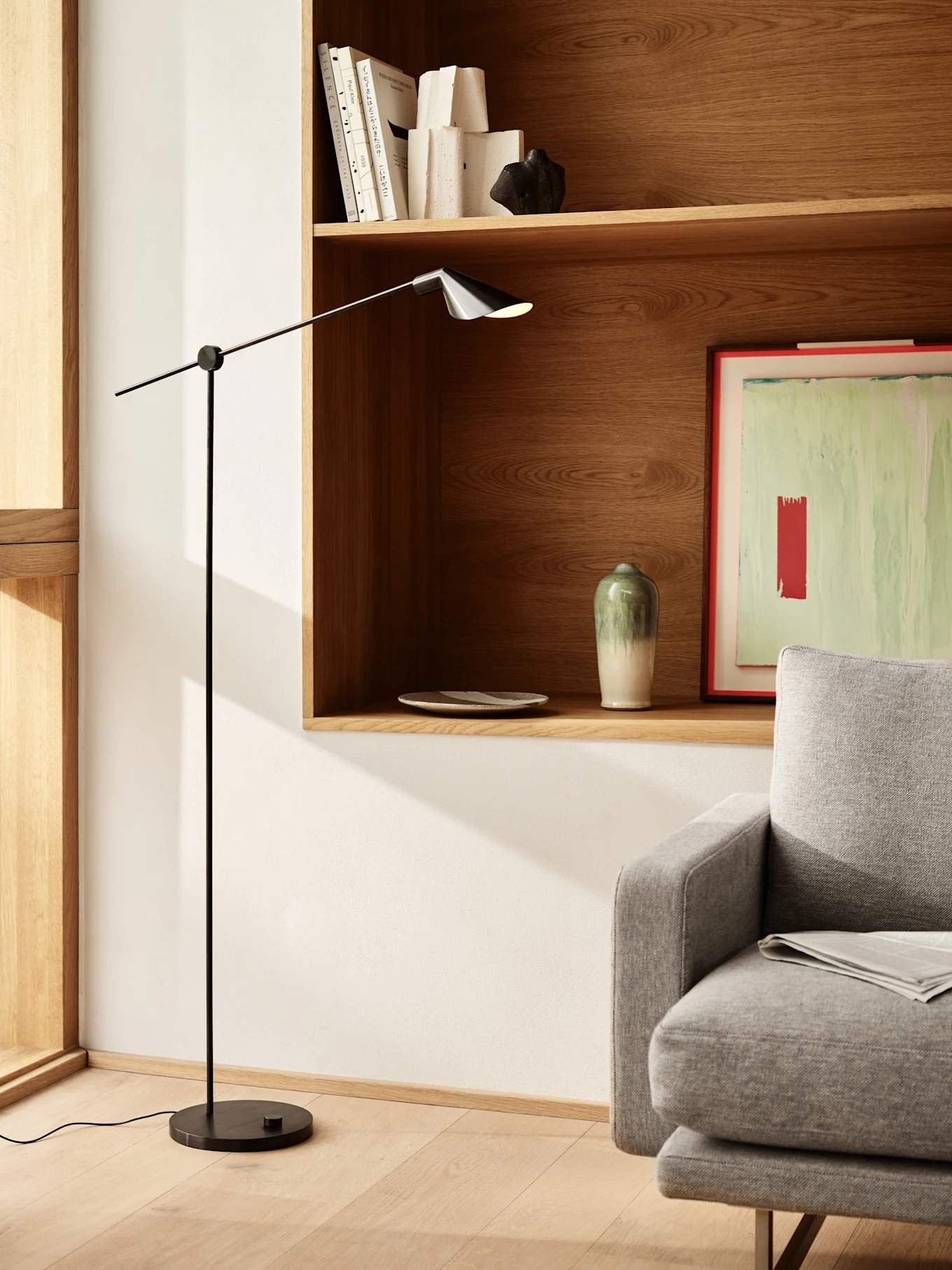Et moderne stuemiljø med en elegant svart gulvlampe, trehyller med bøker og dekor, og en del av en grå sofa.