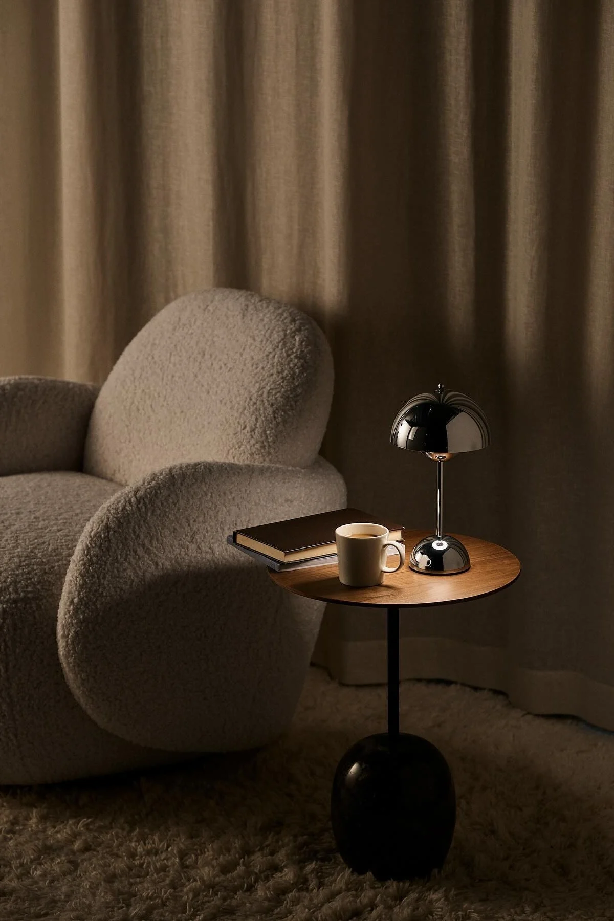 Ved siden av lenestolen Mo fra 1898 står et sofabord med en bok, en kopp kaffe og den kromfargede Flowerpot bordlampen fra &Tradition.
