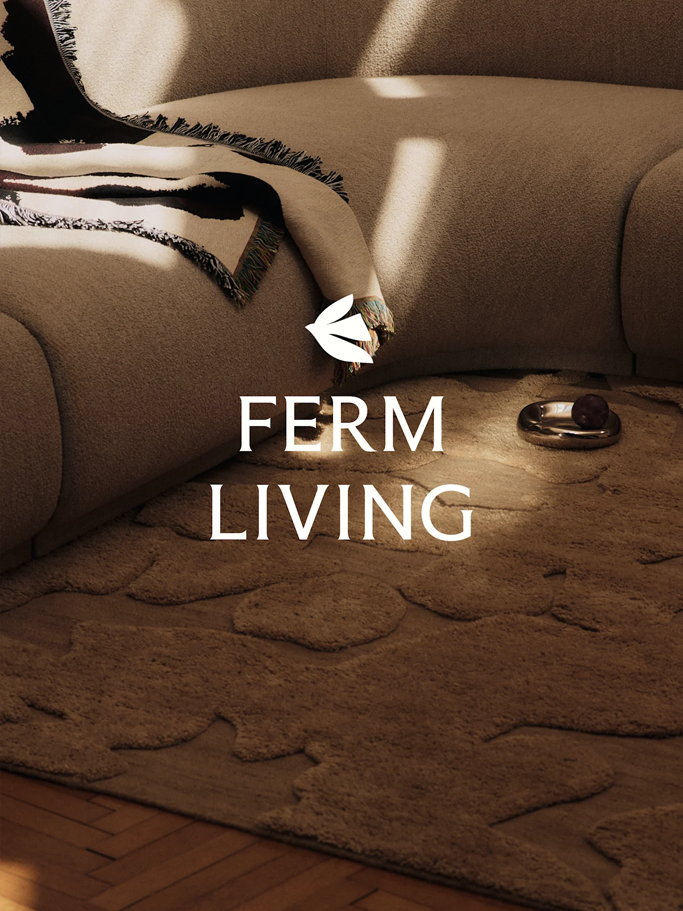 En koselig scene med en lys brun teksturert sofa, et mønstret teppe, et brunt teppe med organiske former og en dekorativ skål.