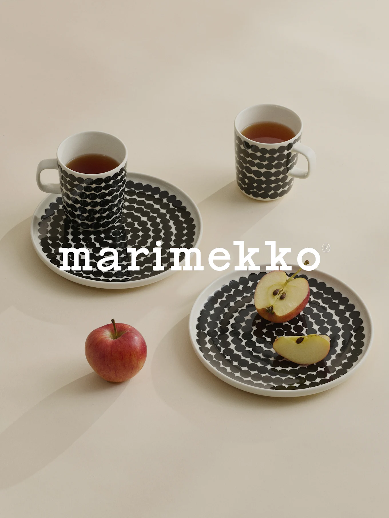 To krus og tallerkener med sorte prikker, te, rødt eple, Marimekko-logo.