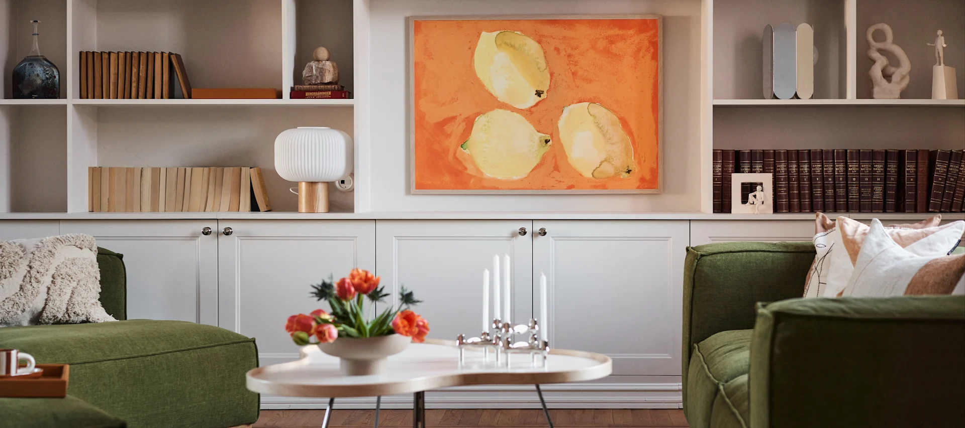 Interiørtrender 2024 - stue med grønn sofa, Swedese-bord, plakater med malt uttrykk og stilig bokhylle.