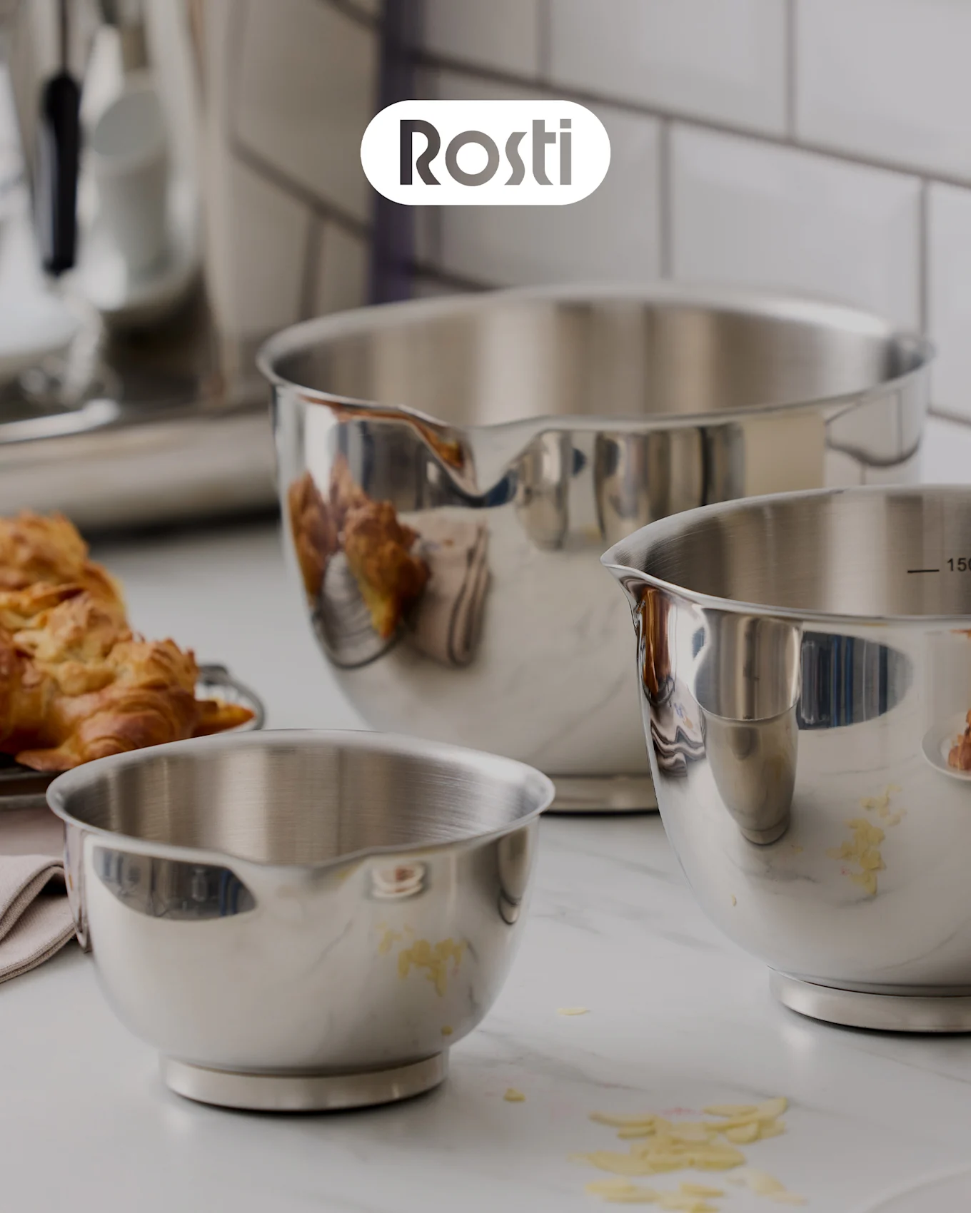 Tre Rosti-skåler på en benk: en beige skål med en blå stablet oppå, begge med lokk, og en liten gul skål fylt med tørkede aprikoser.
