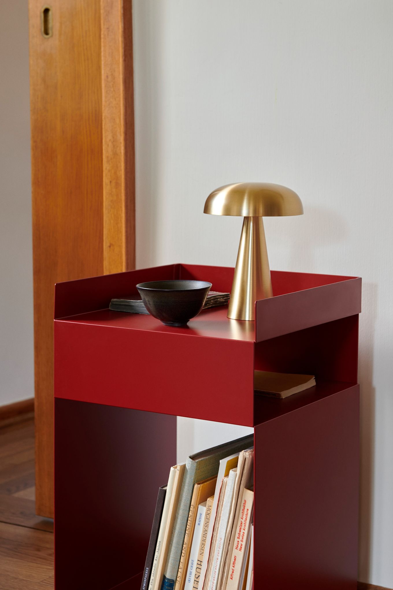 Røde møbler og interiørdetaljer er store innen interiørtrender i 2024 og kan sees her hos &Tradition i form av et rødt sidebord med en liten messinglampe på.