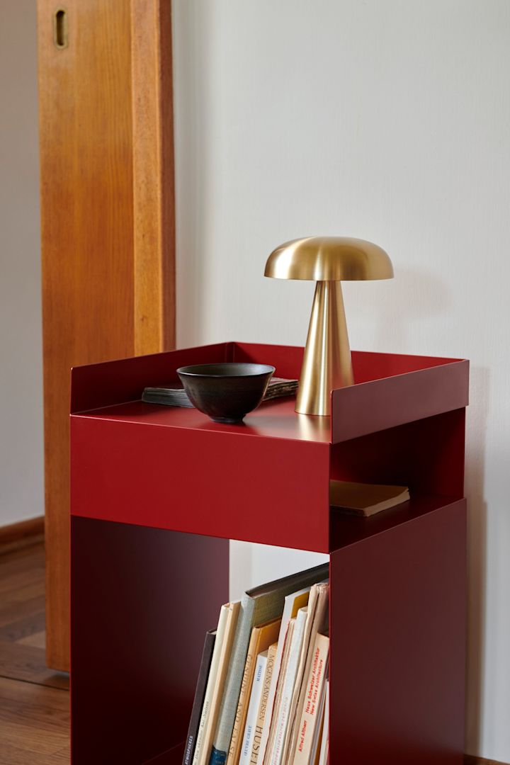 Røde møbler og interiørdetaljer er store innen interiørtrender i 2024 og kan sees her hos &Tradition i form av et rødt sidebord med en liten messinglampe på.