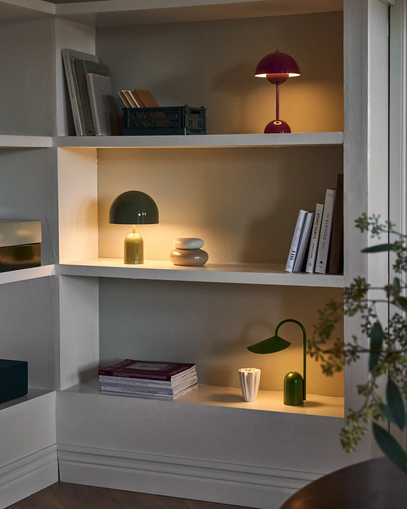 Oplyste hyller i innebygd enhet, med røde og grønne sopplamper, en grønn skrivebordslampe, bøker og dekor.