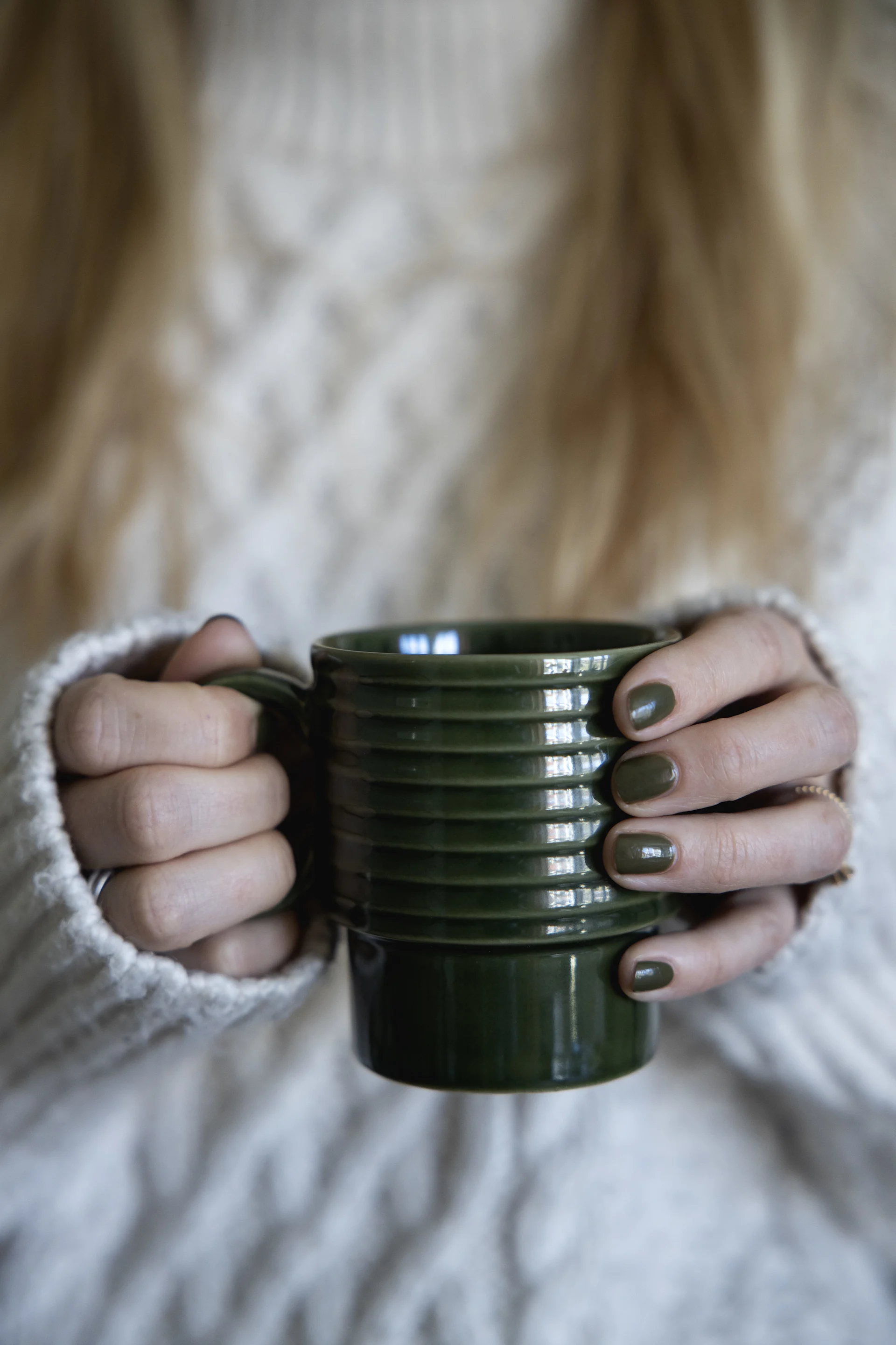 En kvinne i hvit genser holder en grønn kopp fra Sagaforms Coffee & More-kolleksjon i hendene.
