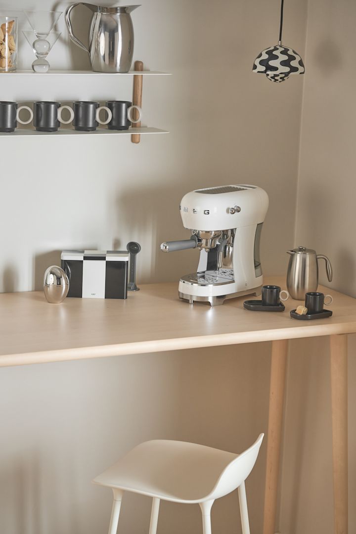 Kaffemaskinen fra Smeg, som du kan se her stående i et hjørne, passer spesielt godt til en kaffebar hjemme, med en Flowerpot pendel fra &tradition som sørger for belysningen.