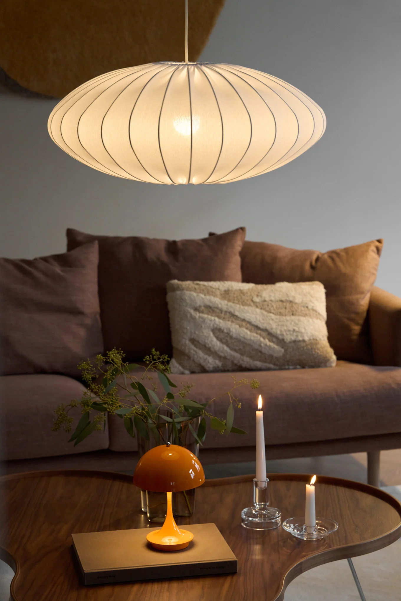 Ellipse-pendellampen med lampeskjerm i stoff fra Watt & Veke henger i en lunt innredet stue.
