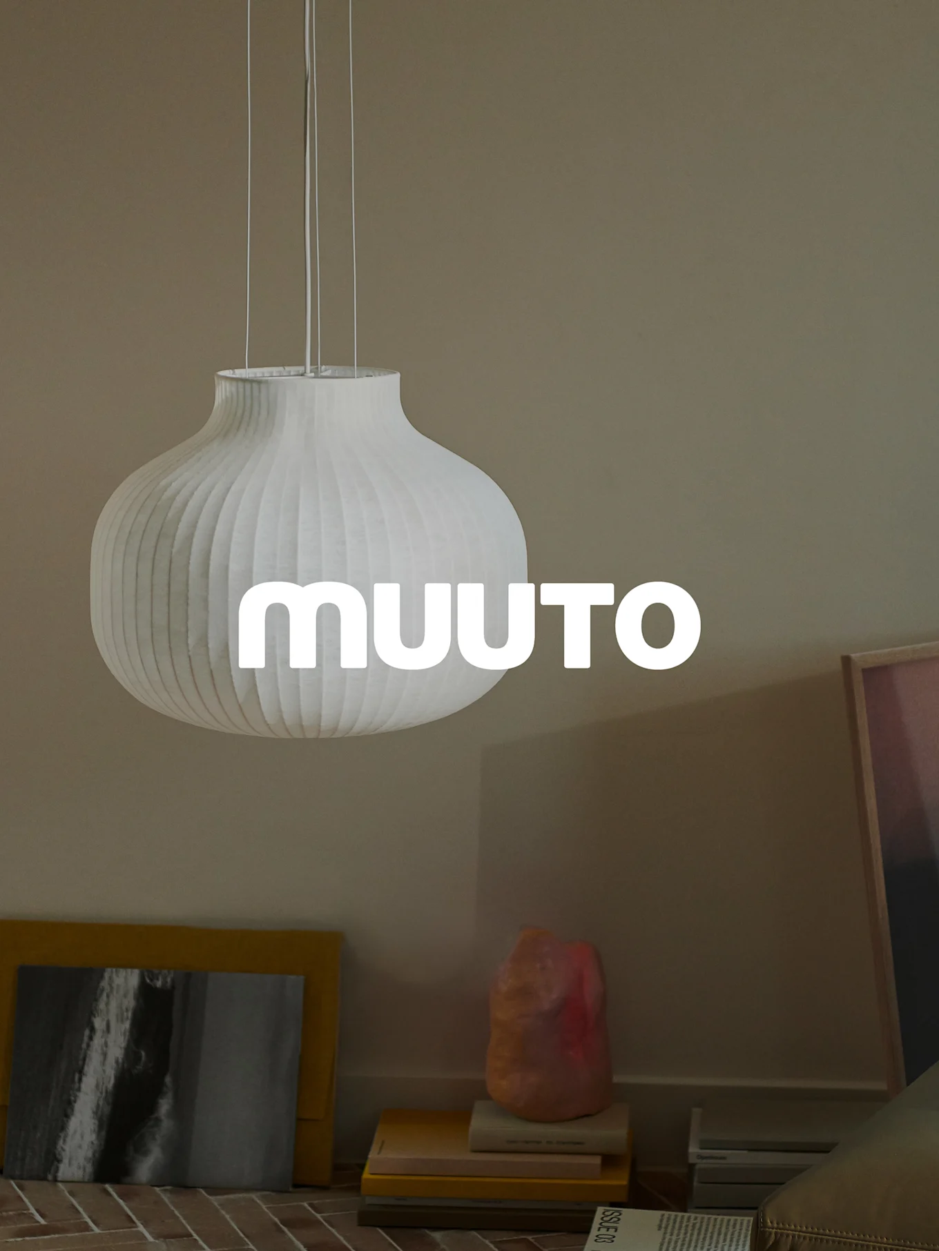 Hvit, ribbet gresskarformet pendellampe med 'MUUUTO'-logo i et beige rom.